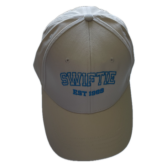 Beige baseball cap with blue embroidery in block text saying SWIFTIE EST 1989